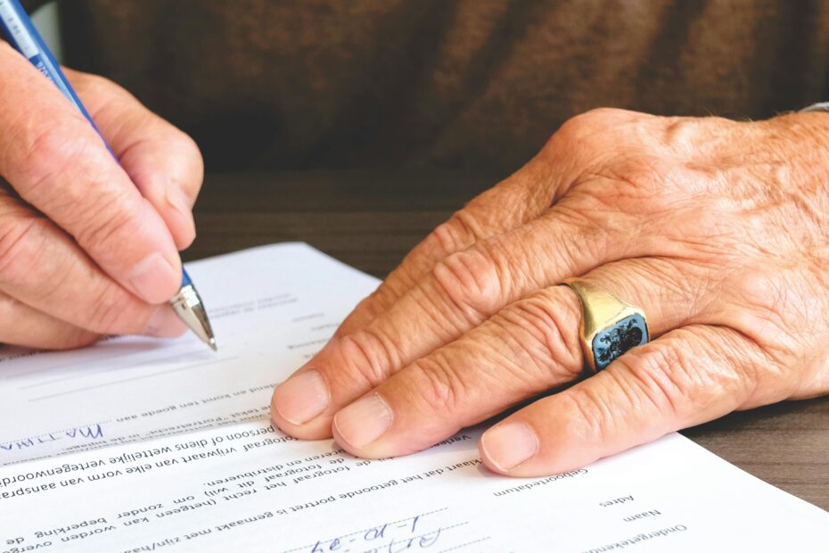 Close-up of a senior adult signing a legal document with a focus on hand and gold ring.