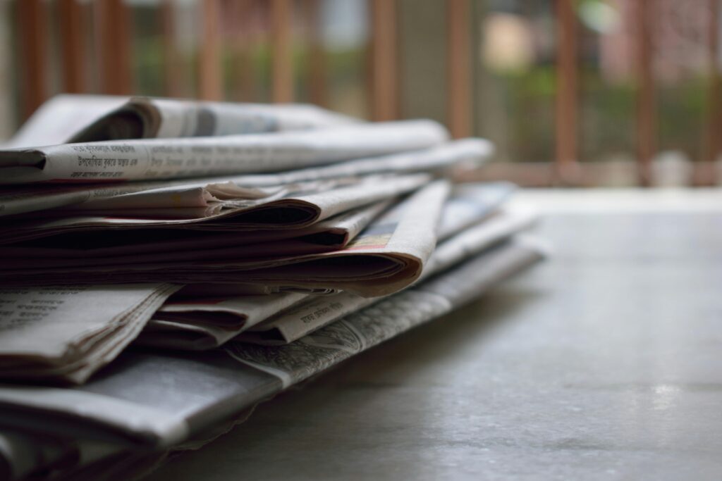 A close-up of a stack of newspapers resting on a desk, symbolizing information and media.