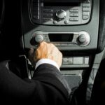Close-up of a driver in a suit operating the car dashboard controls, capturing a professional interior setting.