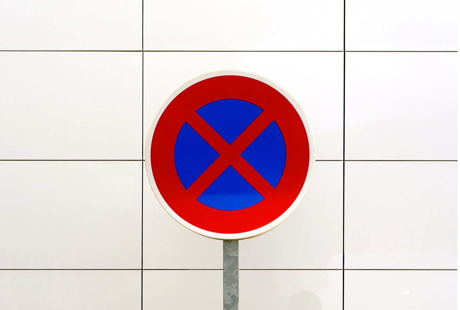 Close-up image of a red and blue no stopping traffic sign against a tiled white background.